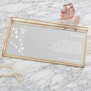May include: A rectangular gold-framed tray with a mirrored surface. The tray features a floral design and the name "Vanessa" with a personalized message. Perfume bottles and a necklace are placed around the tray.