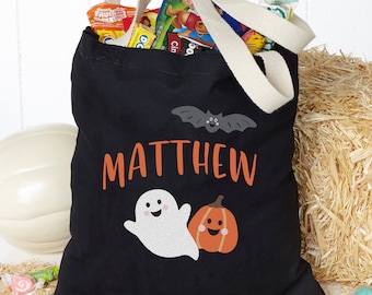 Puede incluir: Una bolsa de tela negra con asas color crema, que presenta el nombre MATTHEW en letras naranjas, un murciélago gris, un fantasma blanco y un gráfico de calabaza naranja. La bolsa está llena de varios paquetes de dulces y aperitivos.