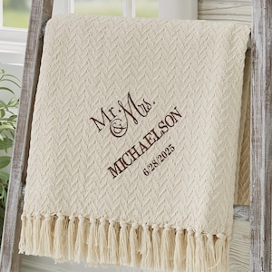 May include: Cream-colored throw blanket with a textured chevron pattern and fringe trim. Embroidered with "Mr. & Mrs. MICHAELSON" and the date "6/28/2025" in brown thread. The blanket is draped over a wooden ladder.