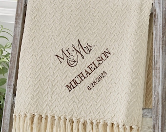 May include: Cream-colored throw blanket with a textured chevron pattern and fringe trim. Embroidered with "Mr. & Mrs. MICHAELSON" and the date "6/28/2025" in brown thread. The blanket is draped over a wooden ladder.