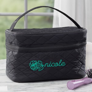 May include: Black quilted makeup bag with a zipper closure and a top handle. The bag has a green embroidered rose and the name "nicole" on the front.