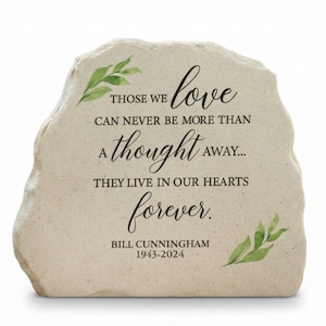 May include: A beige stone memorial with the inscription "Those we love can never be more than a thought away... They live in our hearts forever." Includes the name Bill Cunningham and dates 1943-2024. Features green leaf accents.