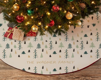 May include: A cream-colored Christmas tree skirt with a repeating pattern of green and gold trees. The skirt has a red border and the text "THE WAGNER FAMILY" in gold. The skirt is under a decorated Christmas tree with ornaments and gifts.