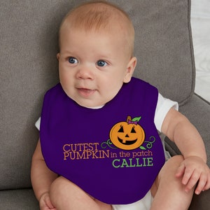 May include: A purple baby bib with the text "Cutest Pumpkin in the patch Callie" and a smiling orange pumpkin graphic. The bib is worn by a baby. The bib is made of soft material.