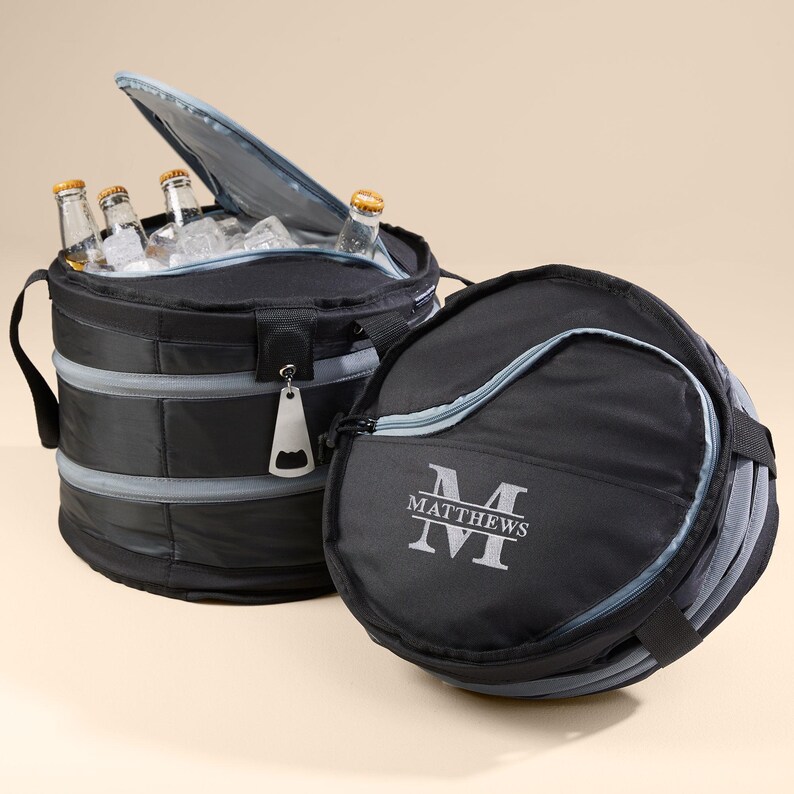 Puede incluir: Bolsa isot&eacute;rmica negra y gris con un bolsillo con cremallera y un abridor de botellas. La bolsa est&aacute; plegada y tiene un monograma personalizado con el nombre "MATTHEWS" y la inicial "M".