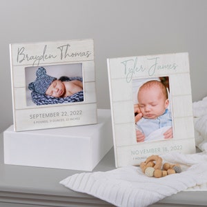 May include: Two white wooden picture frames with baby photos. The frame on the left has the name "Brayden Thomas" and the date "September 22, 2022", with the baby's weight and height. The frame on the right has the name "Tyler James" and the date "November 18, 2022", with the baby's weight.