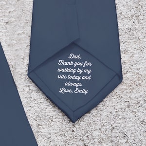 May include: Dark blue tie featuring a heartfelt message. The text on the tie reads: "Dad, Thank you for walking by my side today and always. Love, Emily." The tie is made of a smooth material, suitable for formal wear.