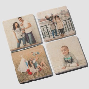 May include: Four square stone coasters featuring custom printed photographs. One shows a family of three, another a couple with a child outdoors, a third depicts a family near a teepee in a field, and the fourth shows a baby sitting on wooden planks.