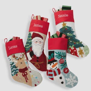 May include: Four Christmas stockings with red cuffs featuring the embroidered names Lucas, James, and Natalie. The stockings display textured needlepoint designs of a reindeer, Santa Claus, a snowman, and a Christmas tree, each filled with small gift boxes.