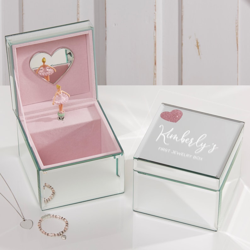 May include: A mirrored jewelry box with a ballerina figurine inside. The lid has a pink glitter heart and the text "Kimberly's First Jewelry Box".