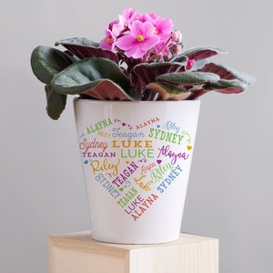 May include: White ceramic flower pot with a heart-shaped design featuring the names Alayna, Riley, Teagan, Sydney, and Luke in colorful lettering.