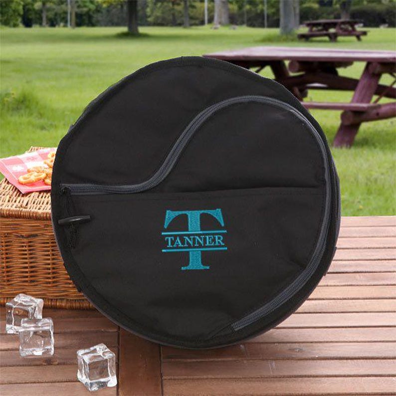 Puede incluir: Bolsa redonda de lona negra con cierre de cremallera y un monograma bordado en azul turquesa que dice "TANNER" en un estilo de fuente dividido.