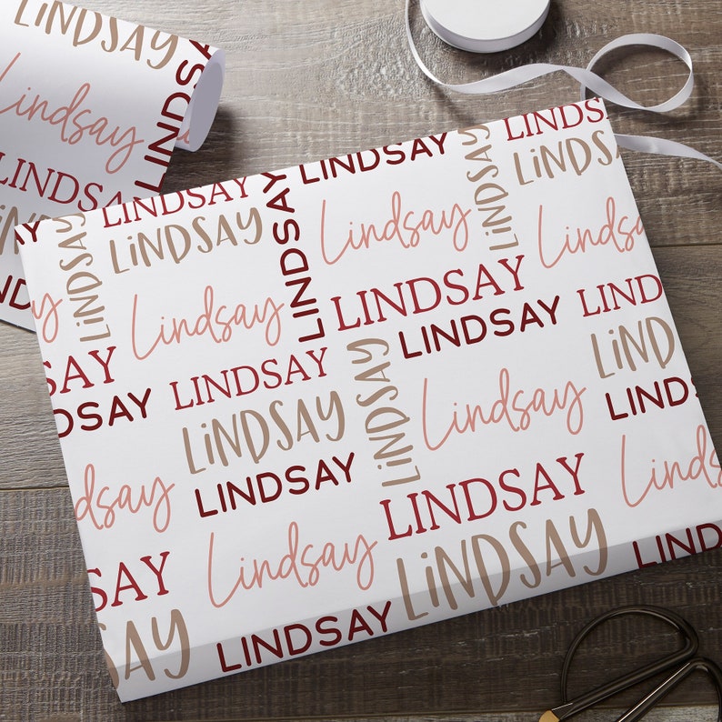 May include: White wrapping paper with the name "Lindsay" repeated in a pattern. The name is printed in both burgundy and light pink.