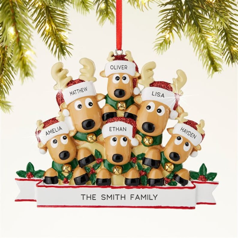 K&ouml;nnte beinhalten: Ein Weihnachtsschmuck mit einer Rentierfamilie. Jedes Rentier tr&auml;gt einen Weihnachtsm&uuml;tze mit einem Namen: Amelia, Matthew, Ethan, Oliver, Lisa und Hayden. Das Ornament hat ein Banner mit der Aufschrift "THE SMITH FAMILY".