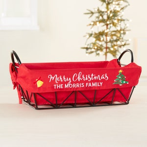 May include: Red and black wire basket with a red fabric liner. The liner has white embroidery that says "Merry Christmas The Morris Family" with a small embroidered Christmas tree and bell.