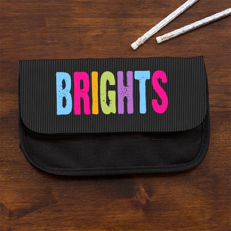 May include: A black pencil case with a textured, vertical-striped flap featuring the word BRIGHTS in large, distressed, multi-colored letters including blue, pink, yellow, green, and purple, accompanied by two white pencils with erasers.