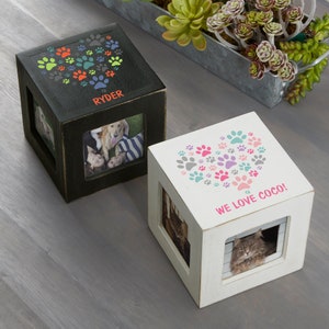 May include: Two wooden photo cubes, one black and one white. The black cube has a paw print heart design and the name "Ryder". The white cube has a paw print heart design and the text "We love Coco!" Each cube has a photo inside.