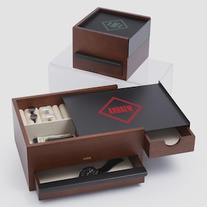 May include: Wooden jewelry box with a black top and drawer pulls. The top of the box has a green logo, and the open box reveals a black interior with the name "ANDREW" in red. The box contains jewelry and a watch.