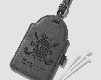 May include: A dark gray rectangular luggage tag with a strap and buckle, featuring a golf-themed engraving that reads Best DADDY By Par, followed by the text We love you, Dad! Love, Jax & Leah, accompanied by three white golf tees.