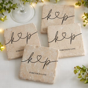 May include: Four square, beige marble coasters with black script initials "k" and "p" connected by a heart. The words "FOREVER IN LOVE" are printed on some coasters. The coasters are on a white surface.