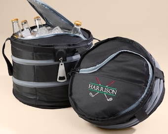 May include: A black and gray personalized cooler bag with a zippered top and a built-in bottle opener. The bag is folded flat and has a golf club design with the name "HARRISON" embroidered on it.