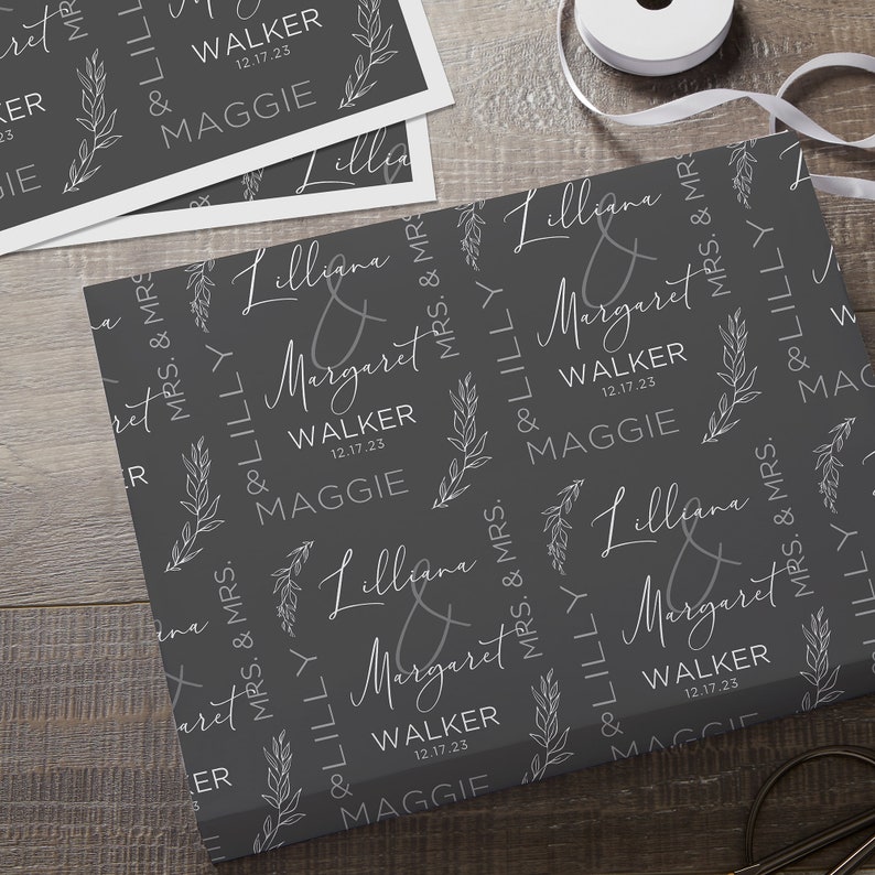 May include: Gray wrapping paper with a repeating pattern of white stylized floral sprigs and the text "Lilliana & Margaret Walker 12.17.23 Maggie" in a script font.