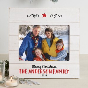 May include: White wooden picture frame with a red star and the text "Merry Christmas The Anderson Family 2022". A family photo is displayed in the frame.