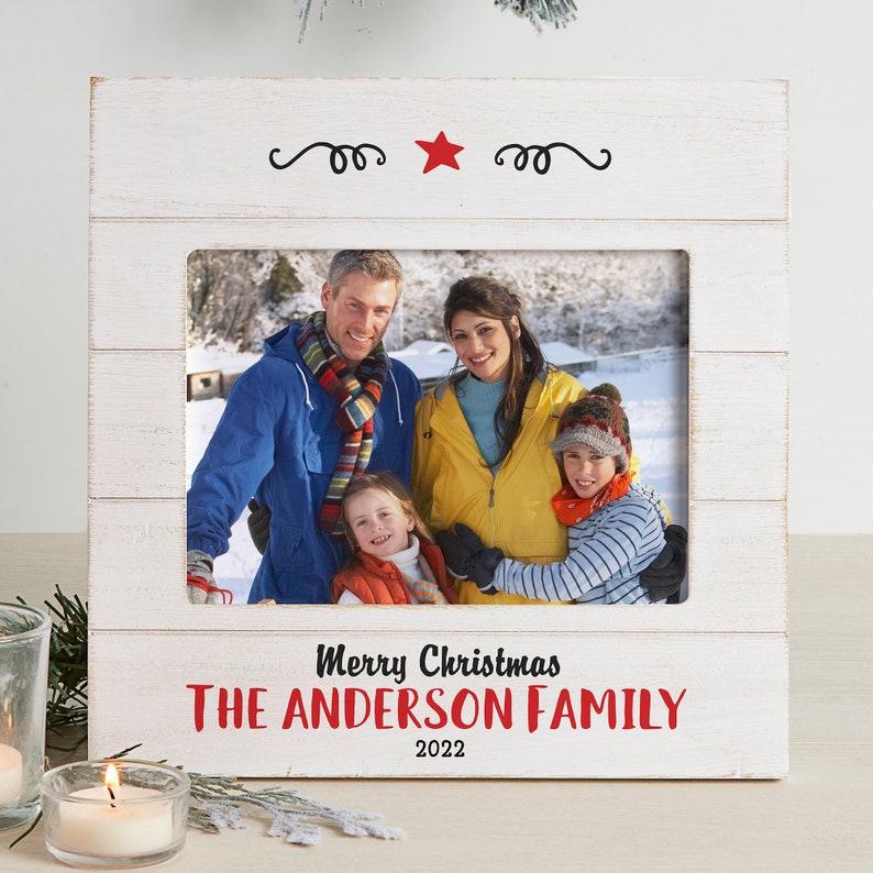 May include: White wooden picture frame with a red star and the text "Merry Christmas The Anderson Family 2022". A family photo is displayed in the frame.