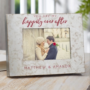 May include: A white wooden picture frame with a distressed finish. The frame has a red inscription that reads "You are my happily ever after."  The frame also has a red inscription at the bottom that reads "Matthew & Amanda".