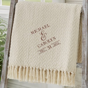 May include: A cream-colored woven throw blanket with a fringe border. The blanket is embroidered with the names "MICHAEL & CAROLYN" and the date "DEC. 31 2024".