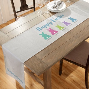 May include: A gray linen table runner with the text "Happy Easter" and four bunny silhouettes with names: Matthew, Lauren, Jackson, and Charlotte. The text "The Wallace Family" is at the bottom of the runner.