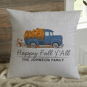May include: A square, light gray pillow with a blue truck graphic carrying pumpkins. The text "Happy Fall Y'all" and "THE JOHNSON FAMILY" are printed below the truck. The pillow has a textured appearance.