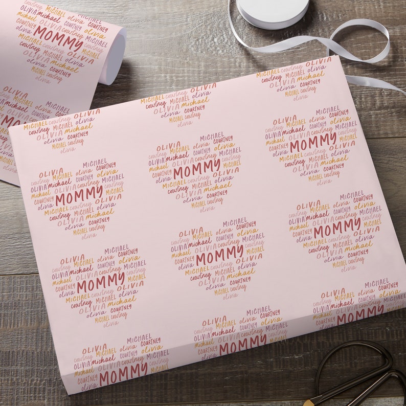 Puede incluir: Papel de regalo rosa con un patr&oacute;n repetido de los nombres "Olivia", "Michael" y "Courtney" en forma de coraz&oacute;n con la palabra "Mommy" en el centro. Los nombres est&aacute;n en color melocot&oacute;n y naranja.