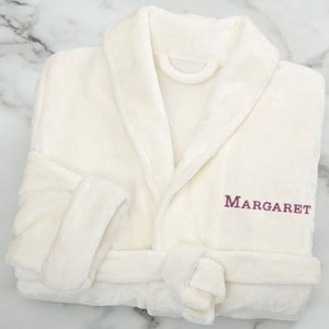 Peut inclure: Peignoir blanc en peluche avec col ch&acirc;le et ceinture &agrave; nouer. Le peignoir est brod&eacute; du nom "MARGARET" sur le devant en fil violet.