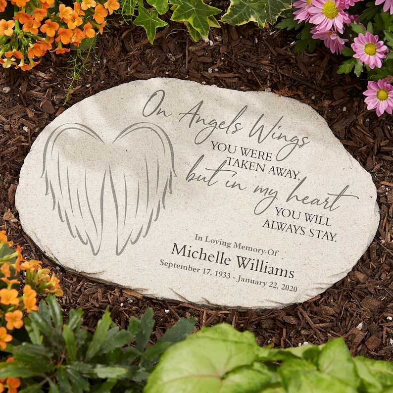 May include: A light gray memorial stone with the inscription "On Angels Wings...but in my heart...you will always stay." Features an etched wing design. In loving memory of Michelle Williams, with dates.