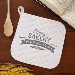 May include: White quilted pot holder with a gray design that says "Emma's Bakery Baked With Love Homemade".