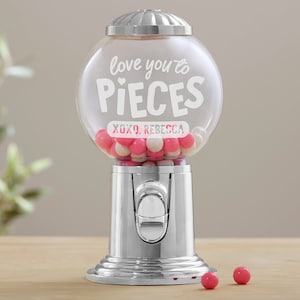 May include: A silver gumball machine with a clear glass globe filled with pink and white gumballs. The globe has a white inscription that reads "love you to pieces xoxo, Rebecca".