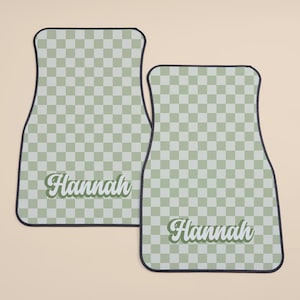 May include: Two green and white checkered car floor mats with black edging. The mats have the name "Hannah" written in a retro font.
