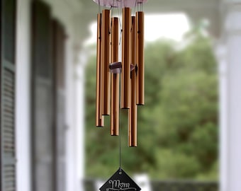May include: A copper wind chime with a black tag that reads "Mom We Love You!" with names listed below. The wind chime is hanging from a wooden ceiling.