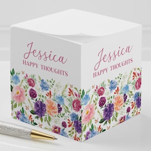 May include: A white cube-shaped notepad with a floral design and the text "Jessica Happy Thoughts" on the front.