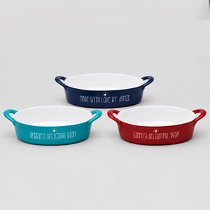 May include: Three oval ceramic dishes in blue, teal, and red, each with white interiors and handles. The blue dish reads "MADE WITH LOVE BY JAMIE", the teal dish reads "DEBBIE'S DELICIOUS DISH", and the red dish reads "GINNY'S DELIGHTFUL DISH".