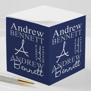 May include: A navy blue cube-shaped notepad with the name "Andrew Bennett" repeated on all sides in a silver-grey font. The name is written in a stylized script font with a handwritten flourish.