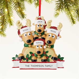 K&ouml;nnte beinhalten: Ein Weihnachtsornament mit einer Rentierfamilie, deren Mitglieder die Namen Anthony, Jack, Megan und Sophia auf ihren M&uuml;tzen tragen. Das Ornament hat ein rotes Band zum Aufh&auml;ngen und einen Banner mit der Aufschrift "THE THOMPSON FAMILY".