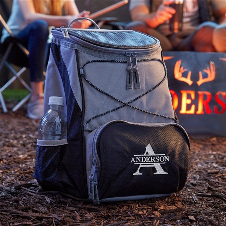 Puede incluir: Una mochila isot&eacute;rmica gris y negra con un bolsillo frontal con cremallera y una letra "A" bordada personalizada con el nombre "Anderson" debajo.
