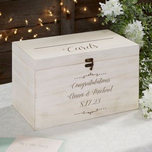 May include: White wooden box with a slot on top for cards. The box has a brass latch and is engraved with the text "Cards", "Congratulations Anna & Michael 8.17.23".