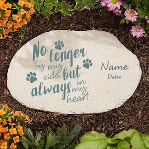 May include: A light-colored stone garden marker with the inscription "No longer by my side, but always in my heart." Paw prints and space for a name and dates are also included. The stone is surrounded by flowers and mulch.