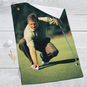 May include: A golfer in a green polo shirt and brown pants is putting a golf ball on a green putting green. He is holding a golf club in his right hand.