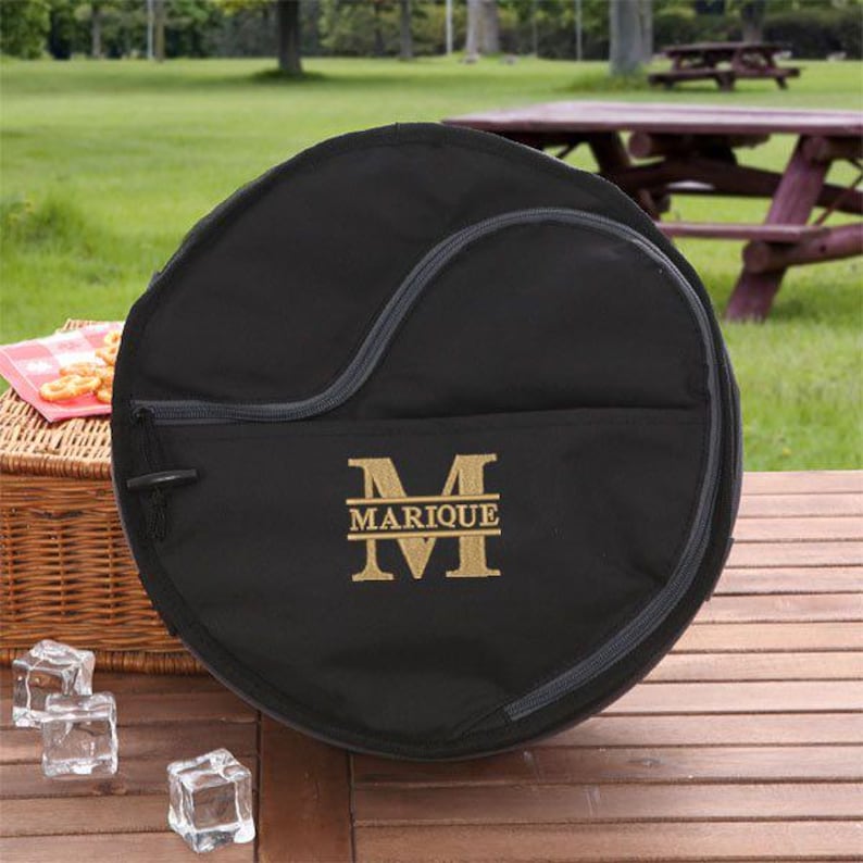 Puede incluir: Bolsa redonda de lona negra con cierre de cremallera y un monograma bordado en oro que dice "MARIQUE" con una "M" grande.