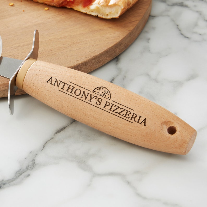 Peut inclure: Un coupe-pizza en bois avec une lame en acier inoxydable. Le manche est grav&eacute; avec "Anthony's Pizzeria" et une petite ic&ocirc;ne de part de pizza.