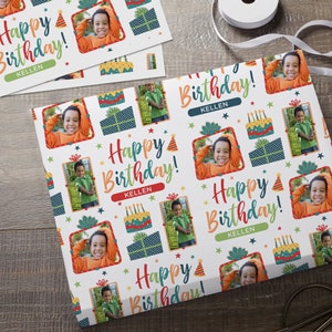 K&ouml;nnte beinhalten: Wei&szlig;es Geschenkpapier mit einem bunten Muster aus Sternen, Geschenken, Geburtstagstorten und Partyh&uuml;ten. Das Papier zeigt den Text "Happy Birthday!" und den Namen "Kellen", der sich wiederholt. Das Papier zeigt auch mehrere Fotos eines jungen Jungen.